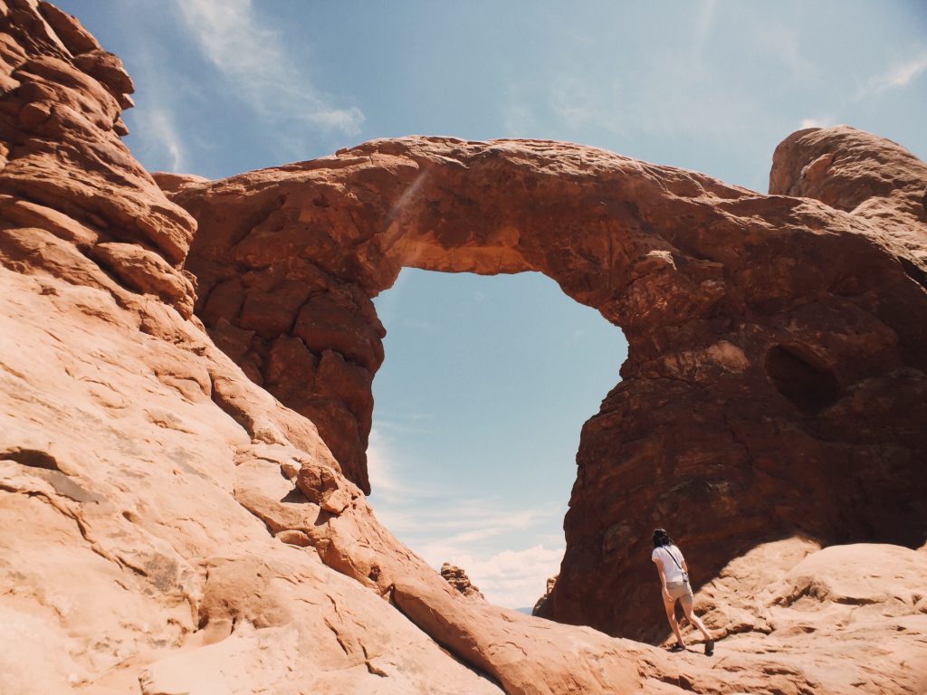 Woman hiking under arch in Arches National Park.