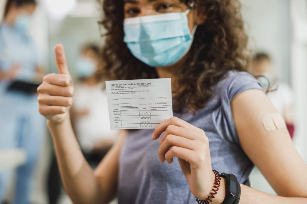 Woman with vaccine card smiling and giving a thumbs up.