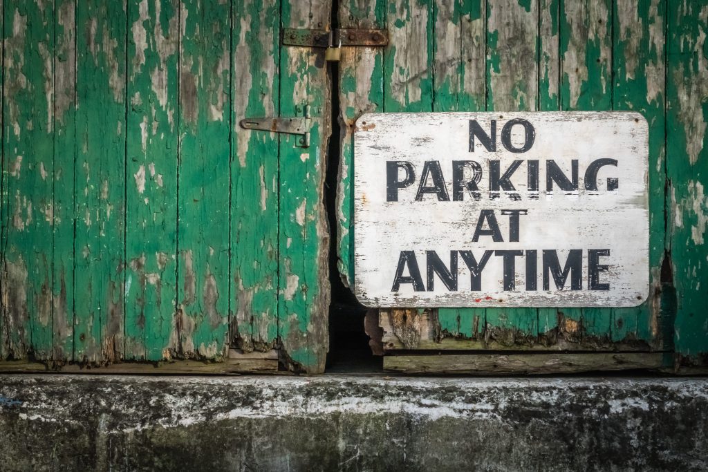 Sign attached to the old green wooden gates of a barrack stating that parking is not allowed at anytime