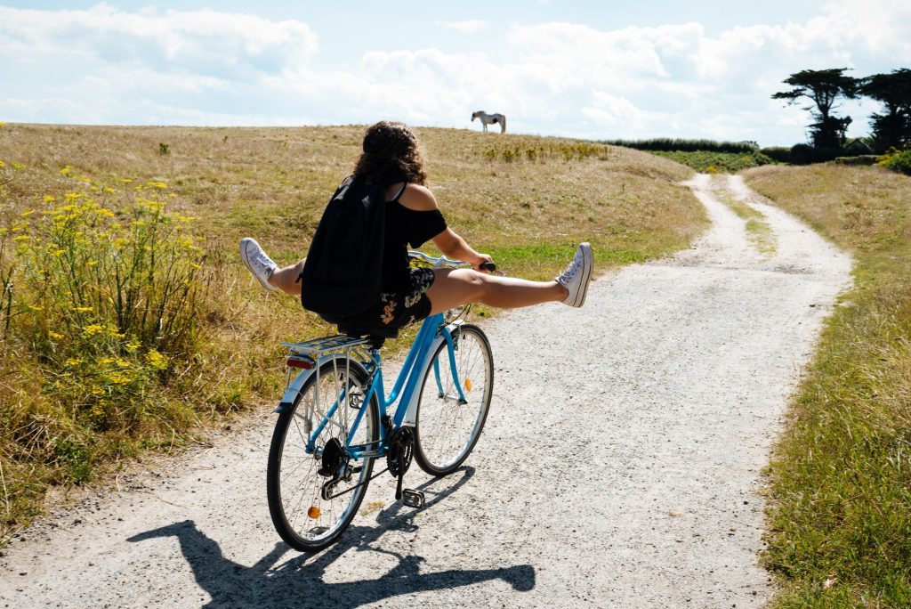 Woman riding bike on dirt road.