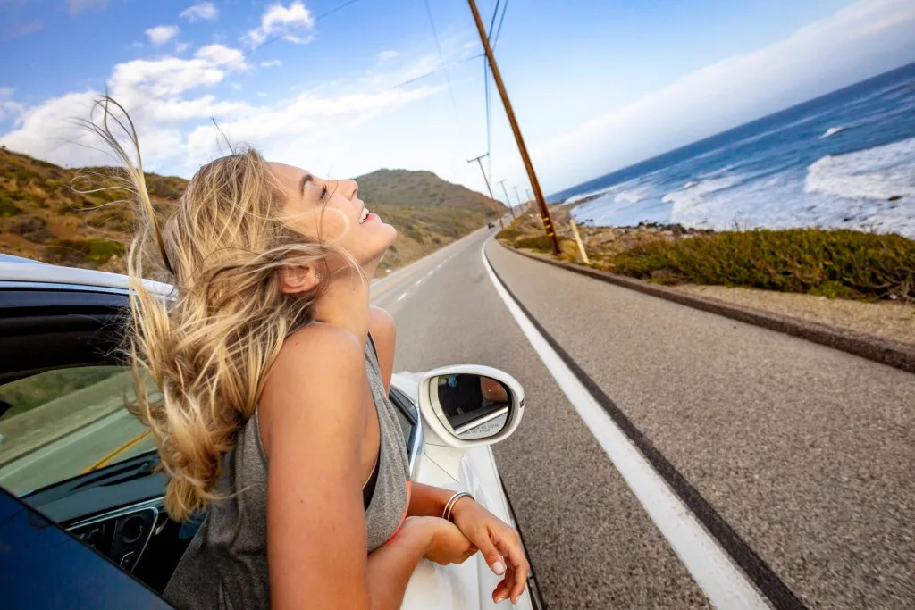 Woman leaning out car window while driving on highway