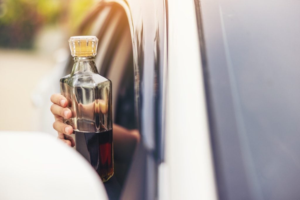 Woman hand holding a bottle of whiskey out of car window.