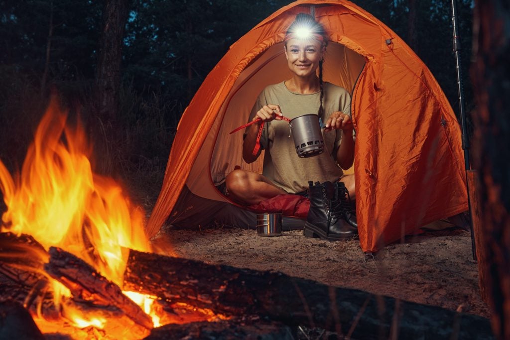 Woman camper sitting in tent by her campfire.