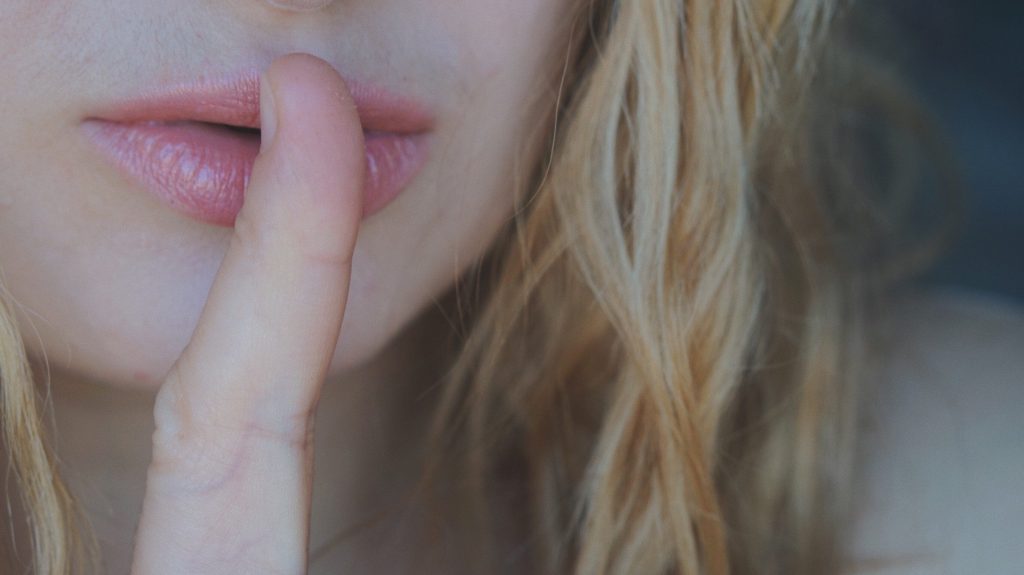 Woman with finger to lips to show a secret.