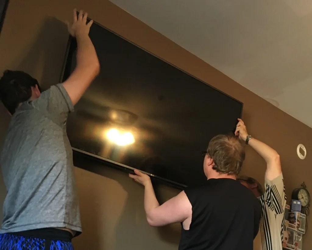 Three men mounting TV together.