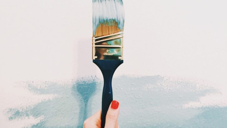 A woman with red fingernails holds a paint brush.