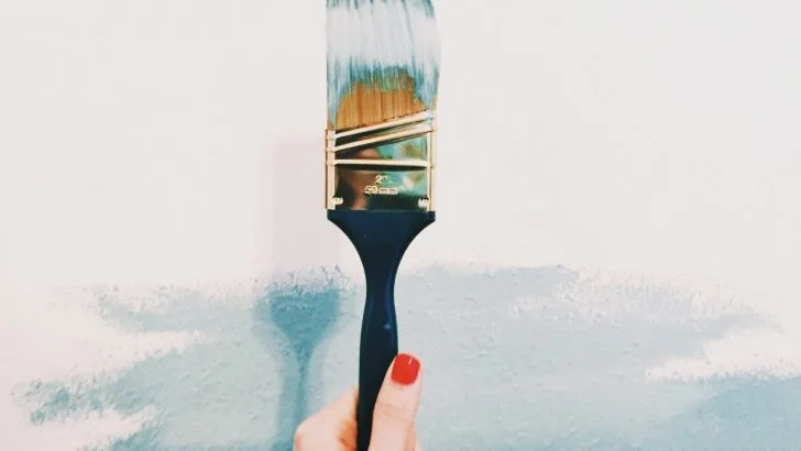 A woman with red fingernails holds a paint brush.