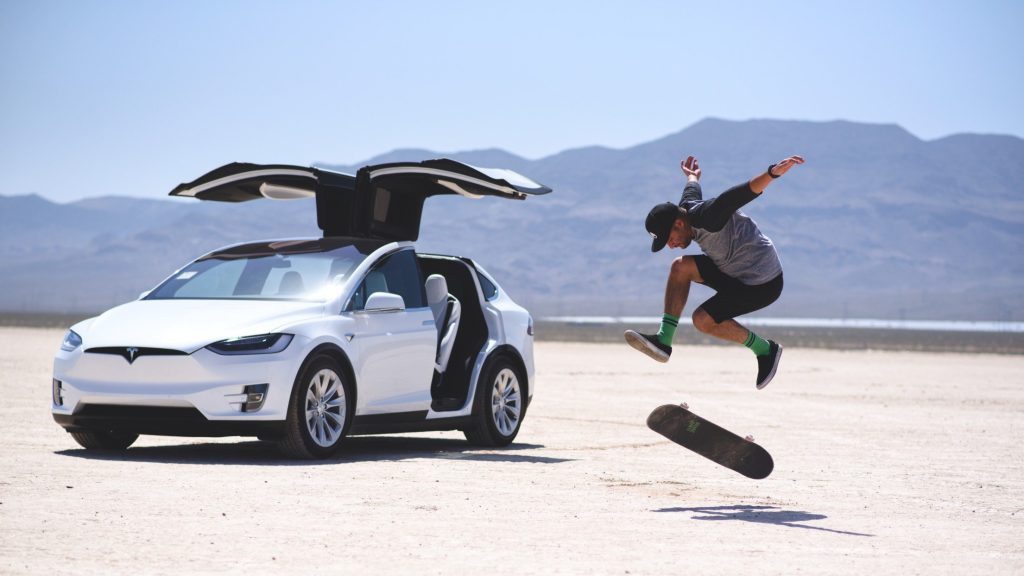 Man skateboarding next to his Tesla.