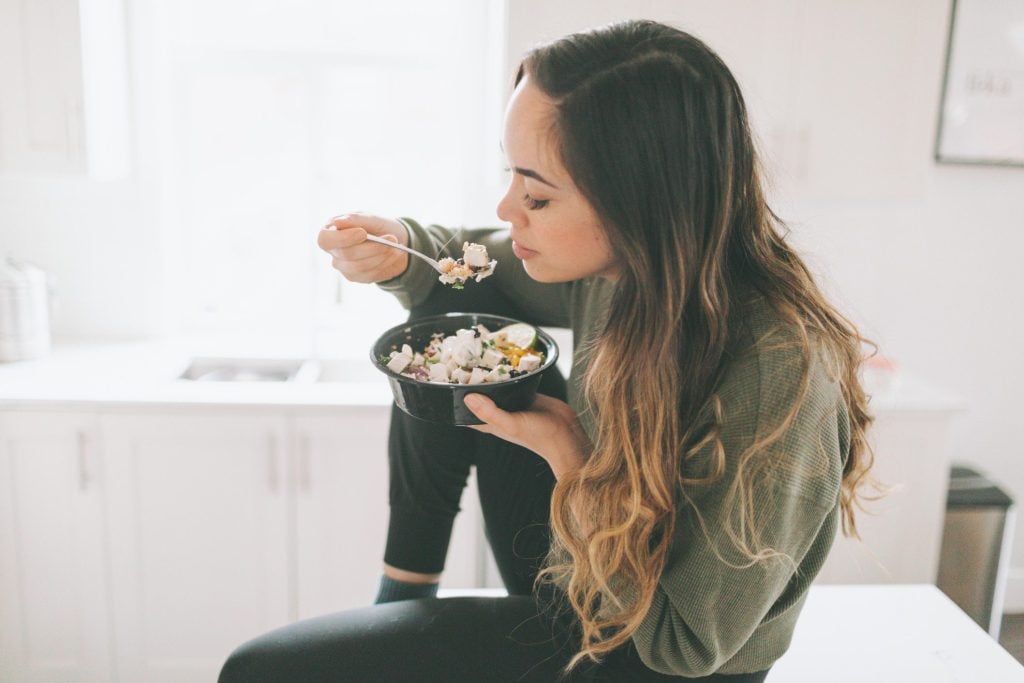 Woman sitting on countertop eating lunch.
