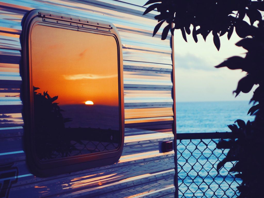 RV window reflecting sunset by beach.