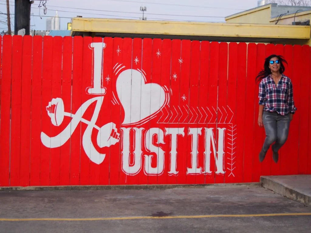 Woman jumping in front of I heart Austin sign.