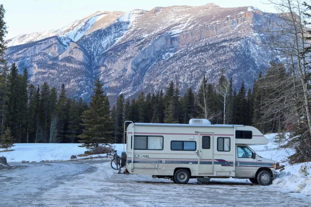 RV parked in the snow by a mountain.