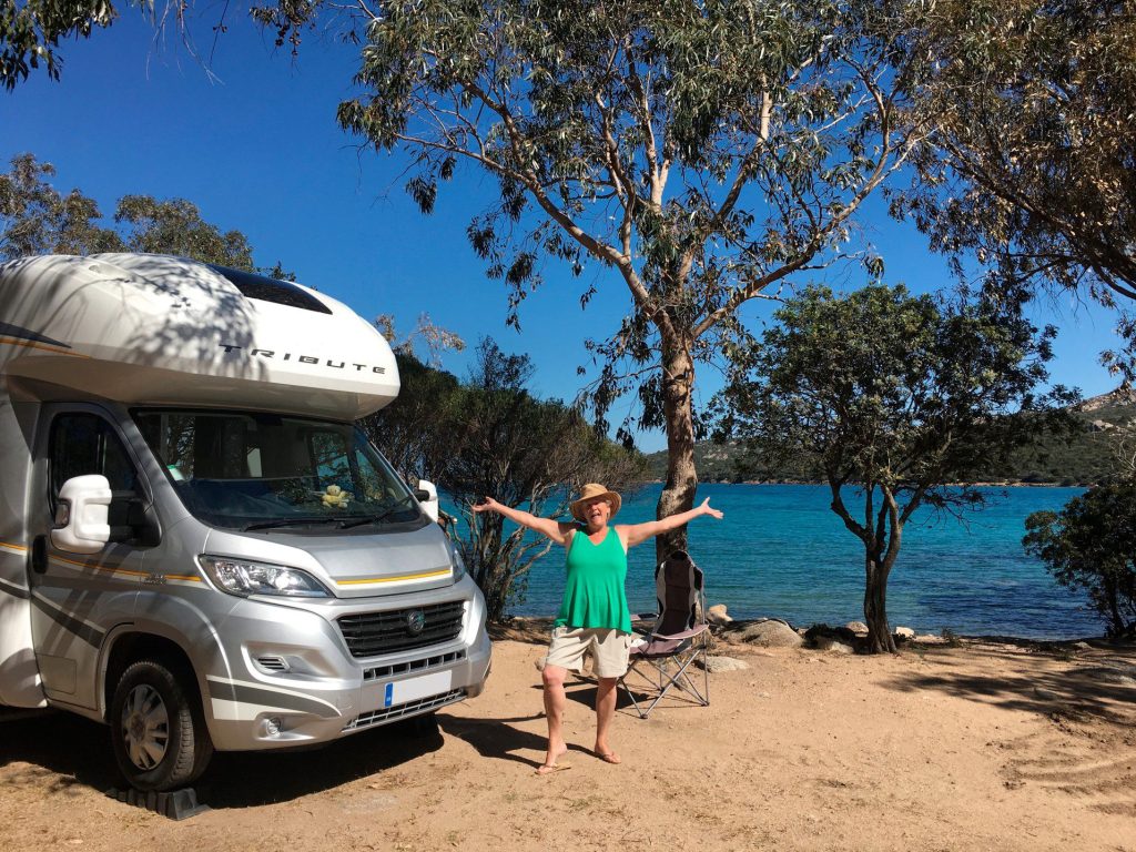 Woman happily posing in front of RV by water.