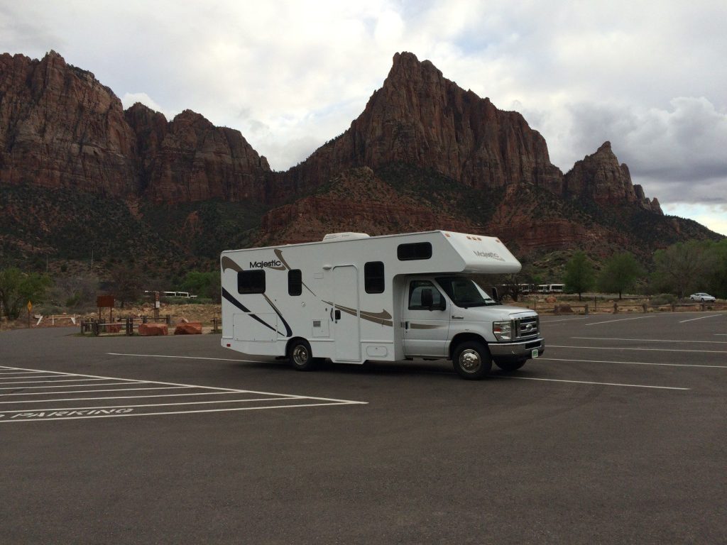 RV parked in parking lot by a mountain.