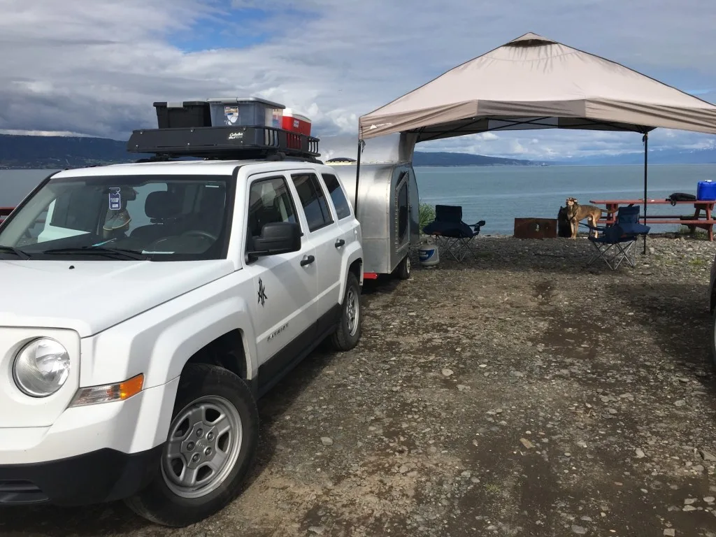 SUV towing teardrop camper parked next to ocean.