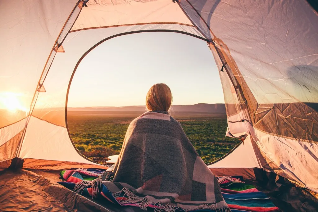 Woman solo camping sitting in tent at sunrise.