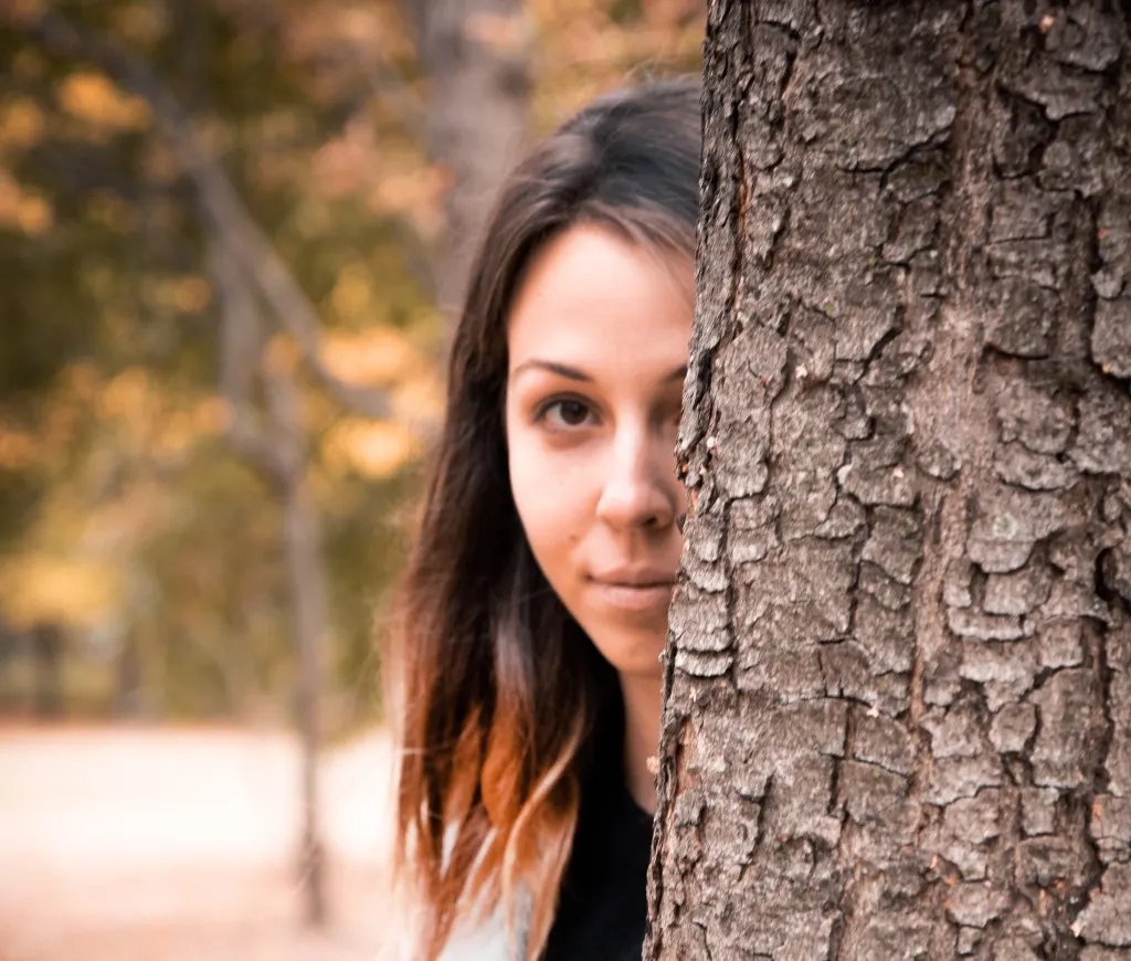 Woman hiding behind tree