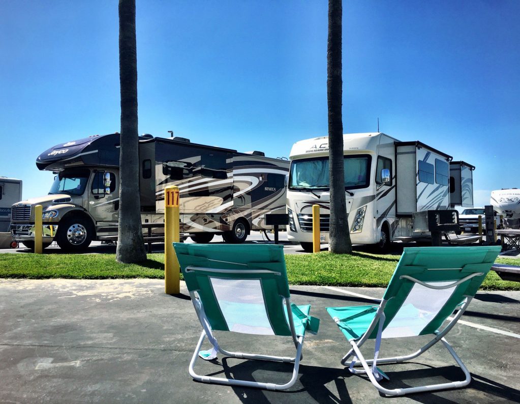 Rv parked in lot with two chairs.