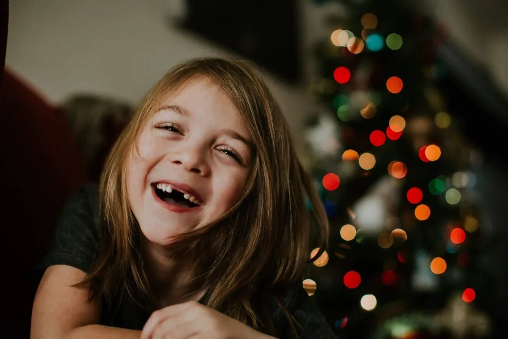 Girl happily posing in front of Christmas tree.