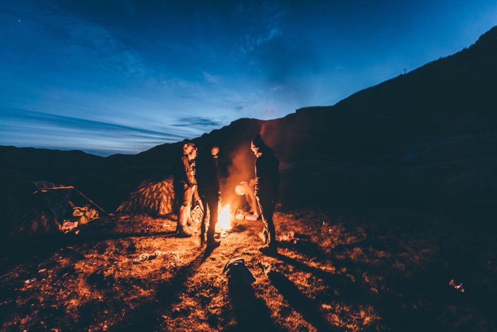 Friends standing around campfire.