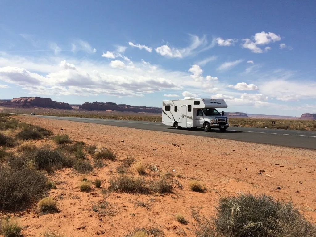 RV driving down road in the desert.
