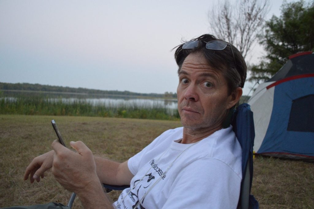Man sitting at campsite on cell phone.