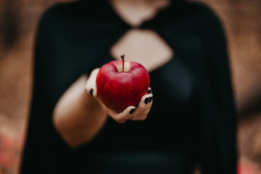 Woman in black cloak holding apple.