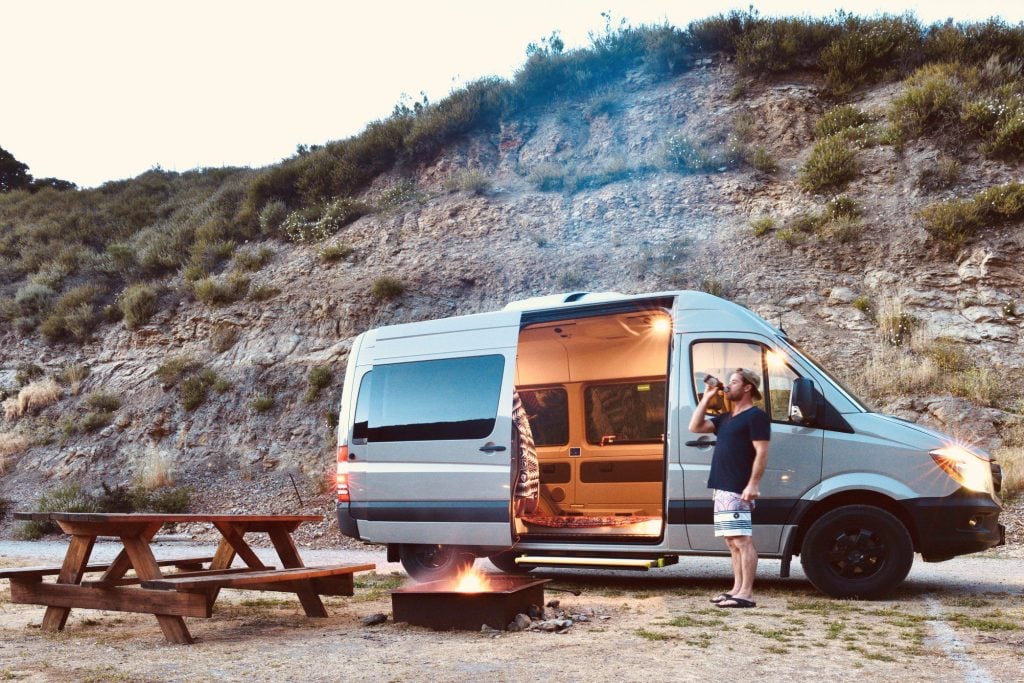 Man drinking beer in front of camper van.