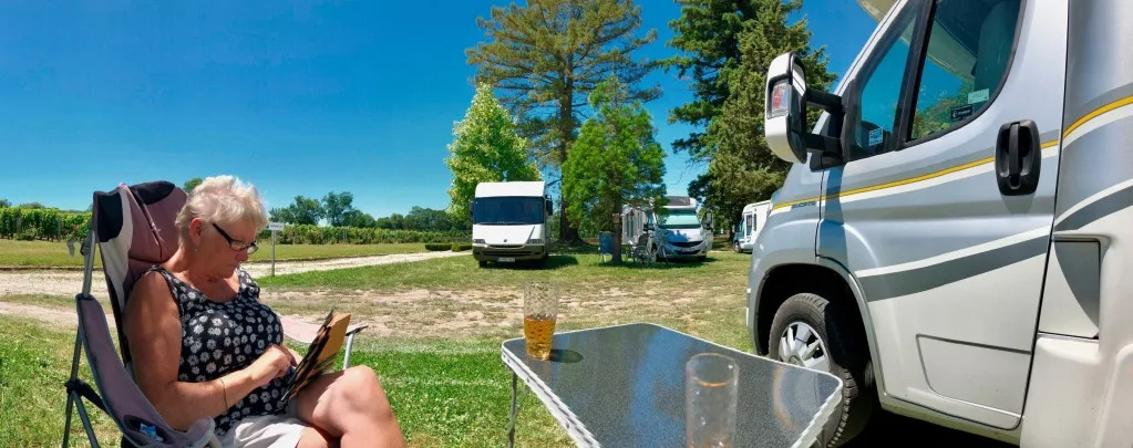 Woman relaxing in front of RV at campsite.