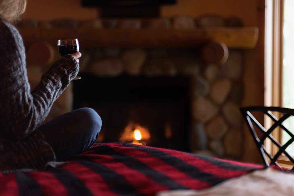 Woman drinking wine in cabin by a fire