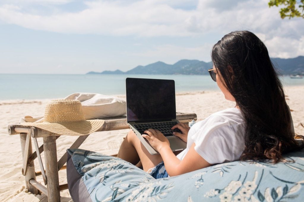 Woman working on laptop from beach.