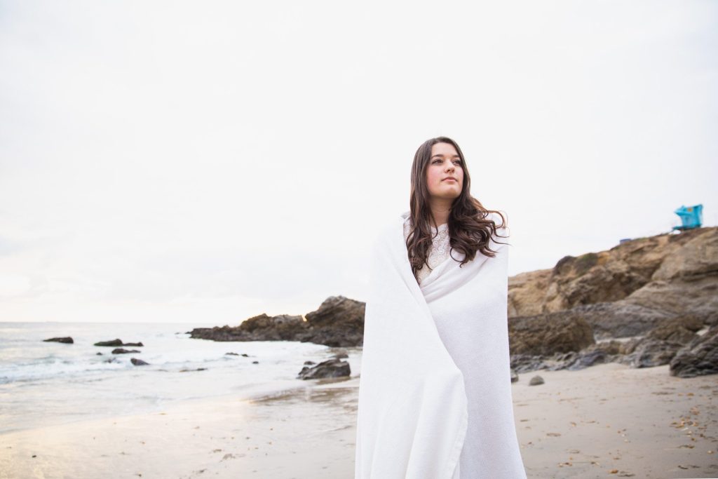 Woman wrapped in towel on California coastal beach.
