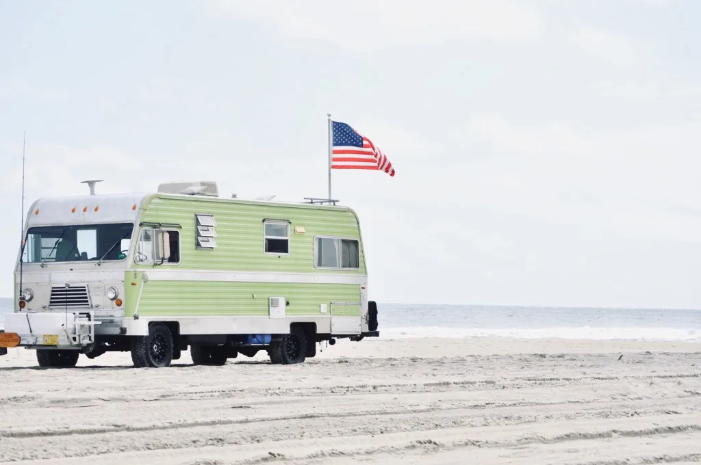 RV parked on beach with an American flag.