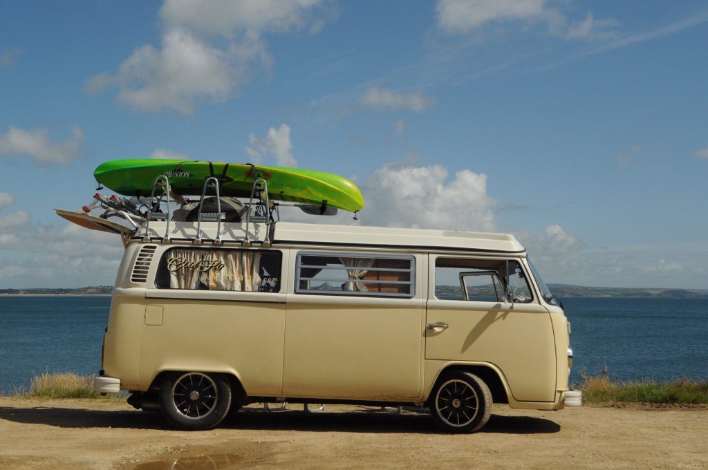 Van with kayak on top parked next to ocean.