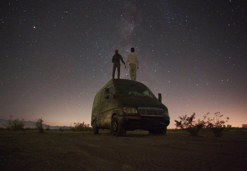Couple standing on sprinter van under the stars.