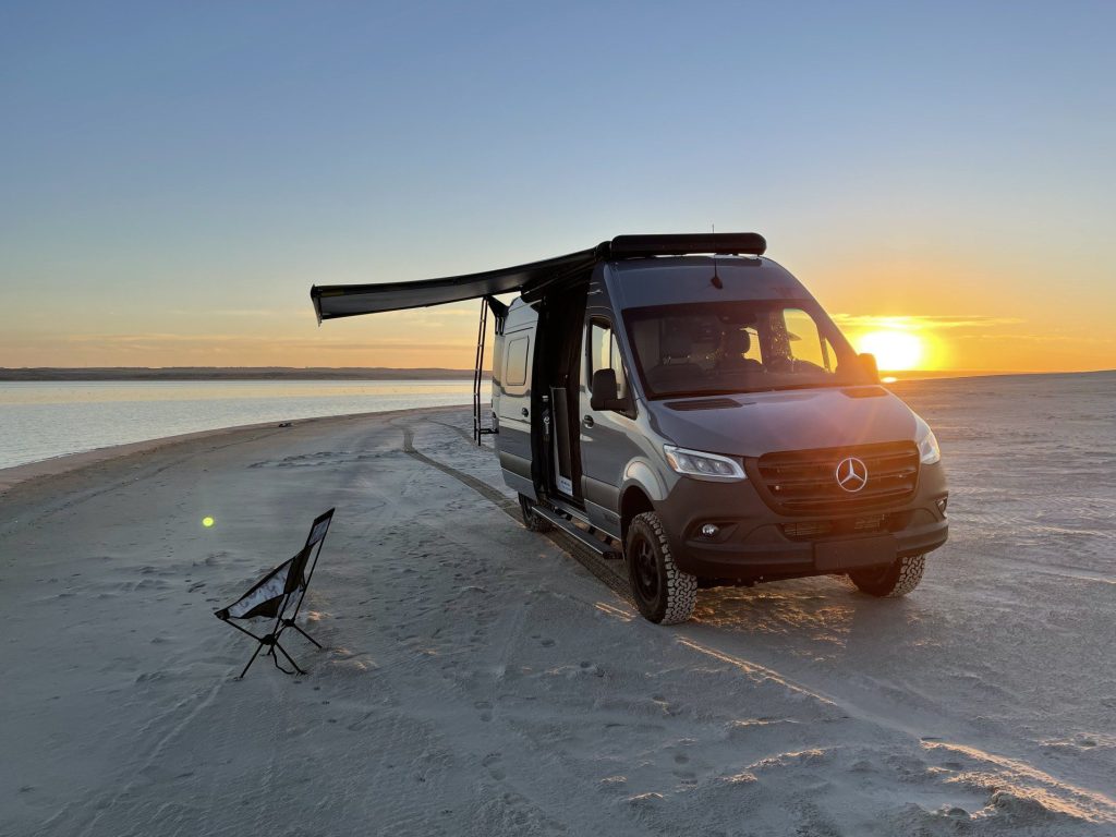 Sprinter van parked on the beach at sunset.
