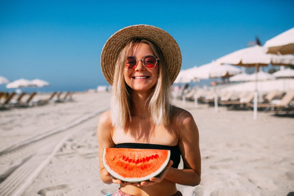 Woman happily eating watermelon on beach.