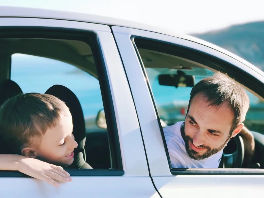 Father and son smiling at each other on a road trip.