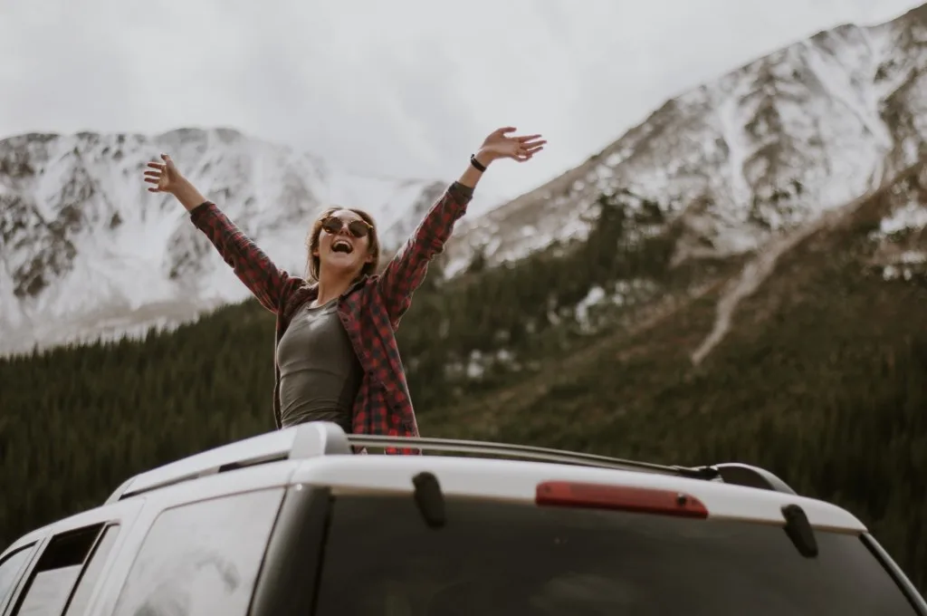 Woman happily out sun roof driving through mountains.