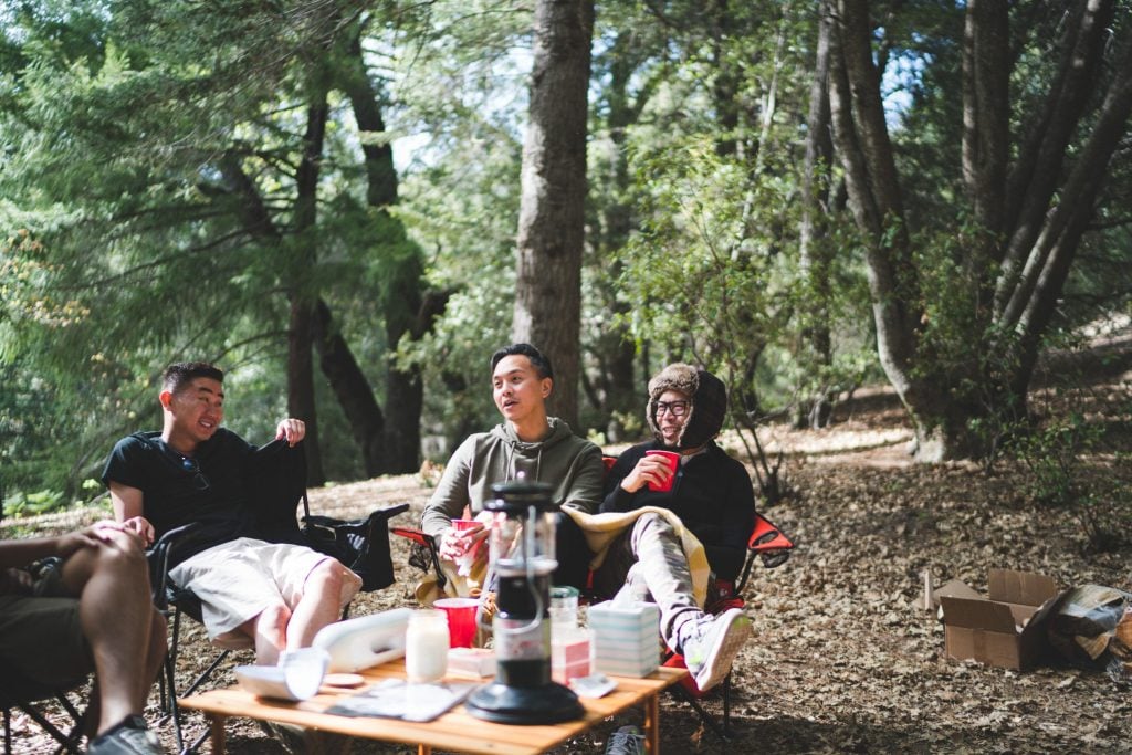 Three friends sitting around campsite.