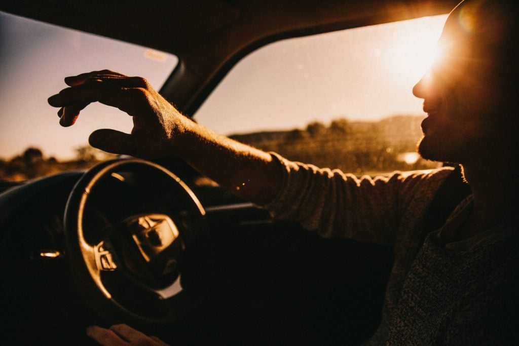 Person happily driving on road trip at sunset.