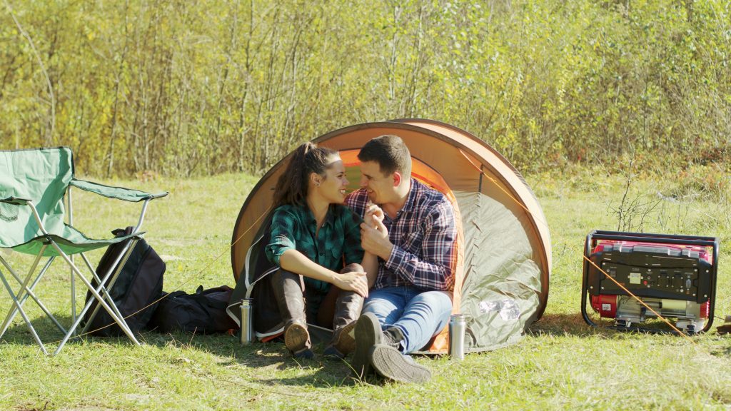 Couple sitting in tent next to camping generator