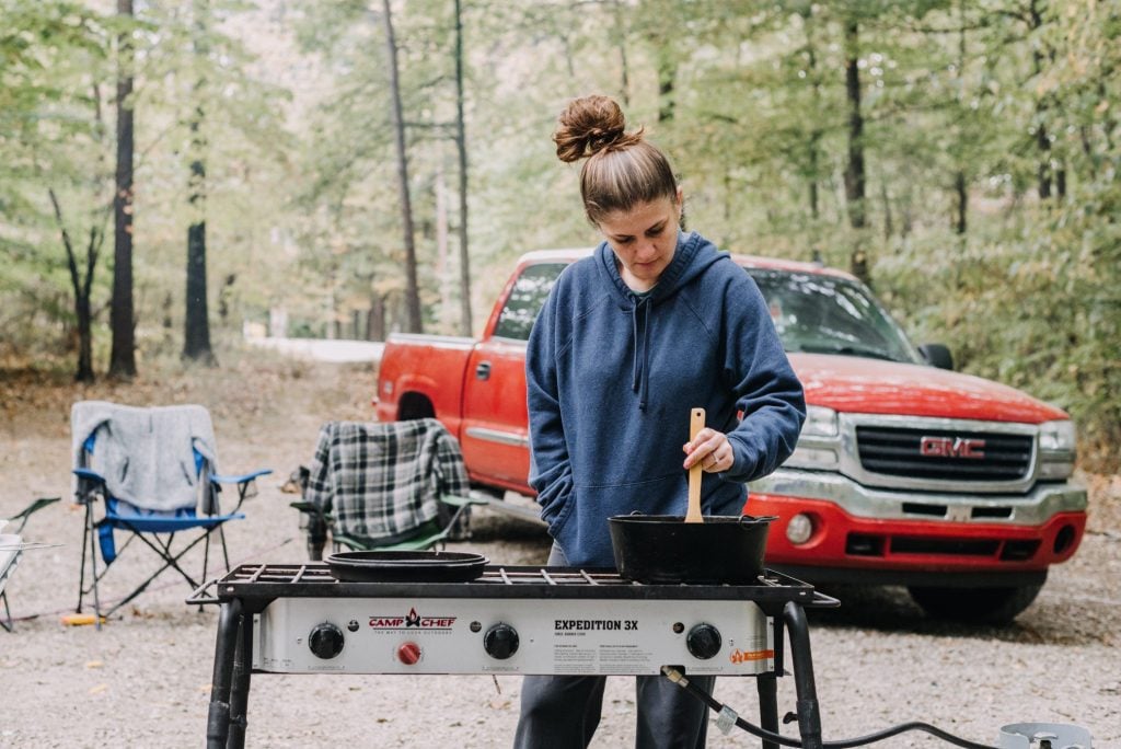 Woman cooking in front of her red truck at campsite.