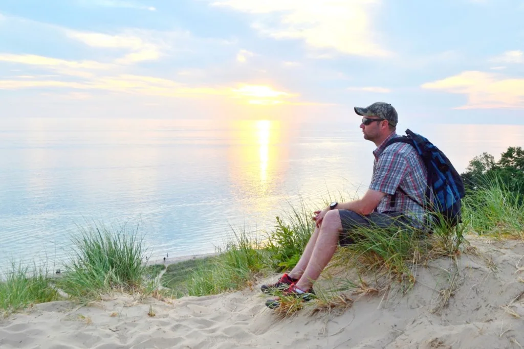 Man sitting on sand dune in Charles Mears State Park while hiking.