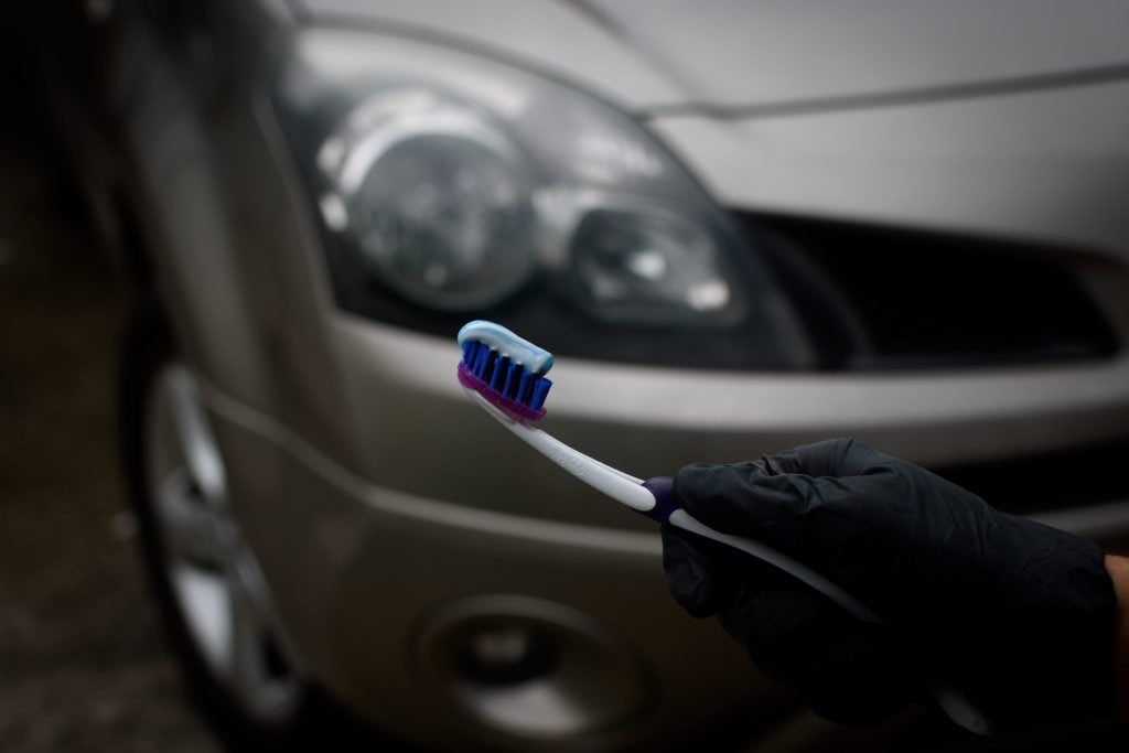 Technician with holding toothbrush and toothpaste to shine and brighten the headlights of the car. Topical car wash and care. car care. headlight polishing and care concept..