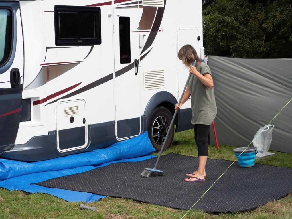 Woman sweeping in front of of motorhome parked at a house.