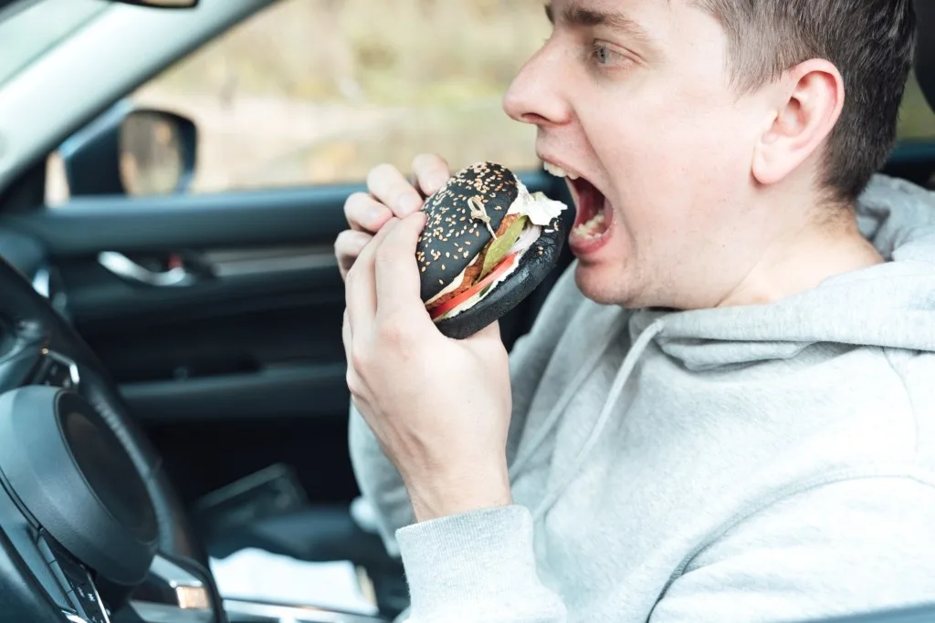 Man eating burger in car while on a road trip