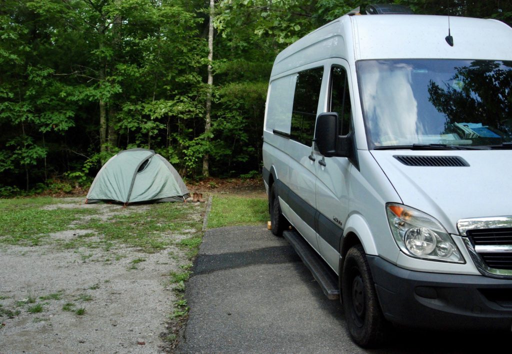 Sprinter van parked at campsite next to pitched tent