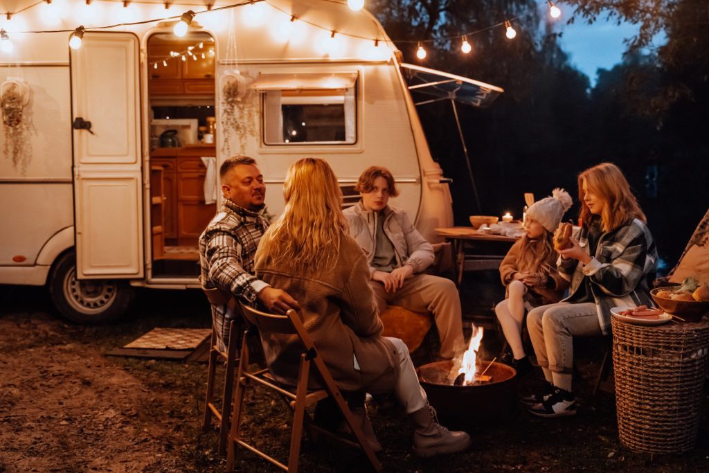 Family sitting around a campfire in front of travel trailer.