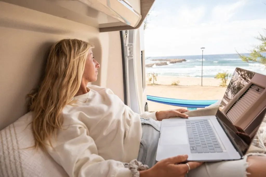 View of woman working on her laptop from a wild camping spot, Sardinia, Italy.